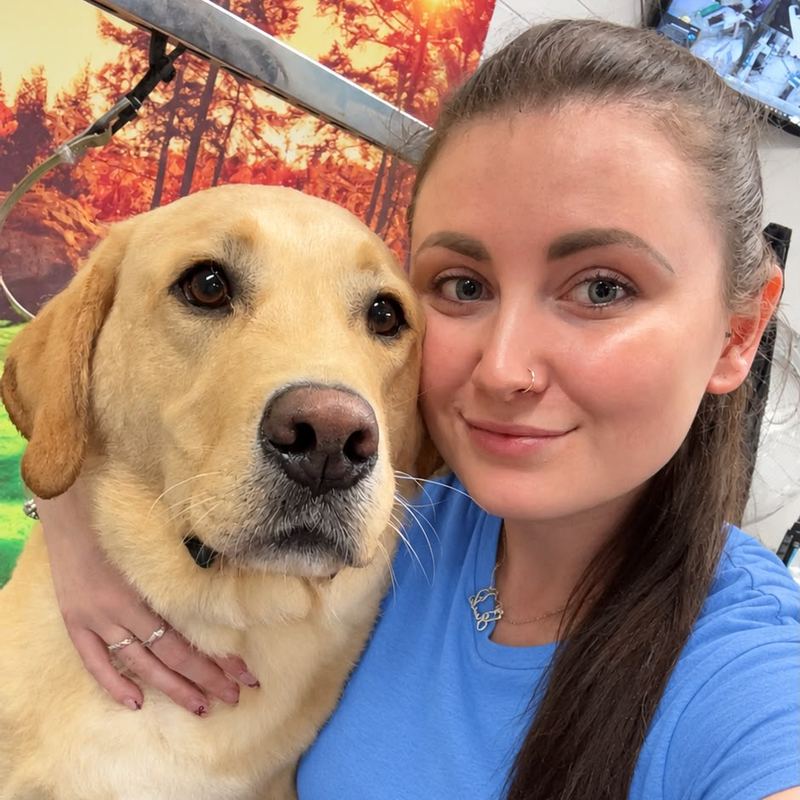 Emily, dog groomer, smiling cheek to cheek with a golden Labrador
