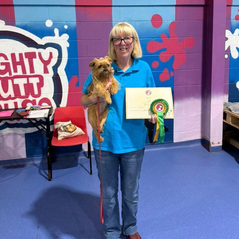 Ruby, dog trainer, holding a small brown terrier with a rosette and certificate