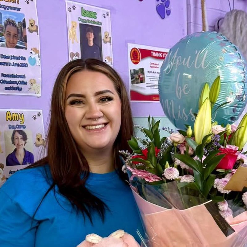 Sophie, supervisor, smiling in front of the staff notice board
