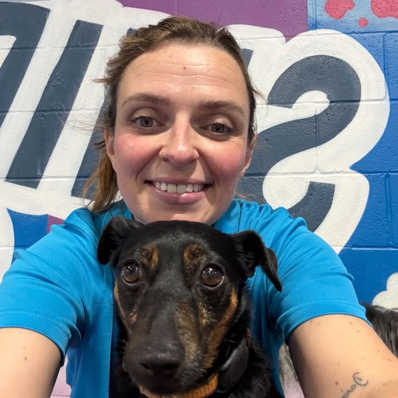 Terri from the day camp team smiling with a black and tan dog